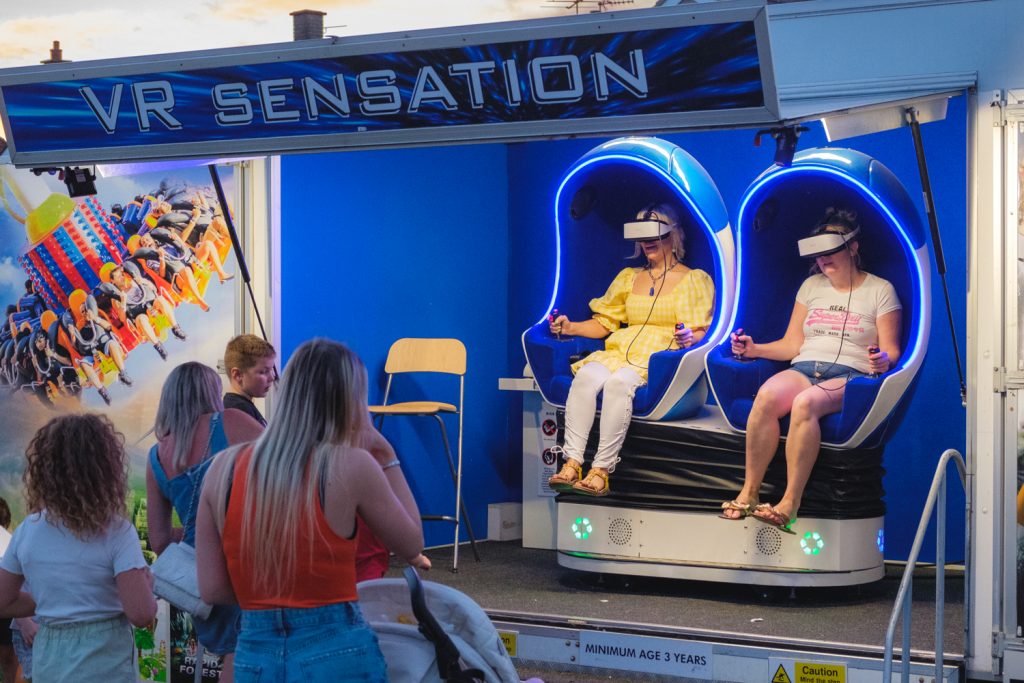 Two people sitting in a a booth with VR headsets on while people watch